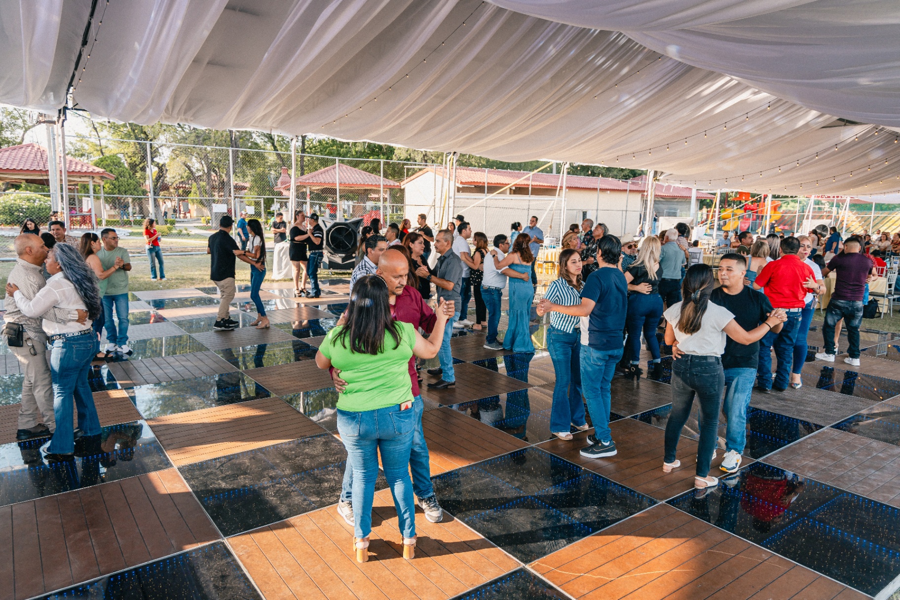 Invitados bailando en pista reflejante bajo carpa con luces colgantes.